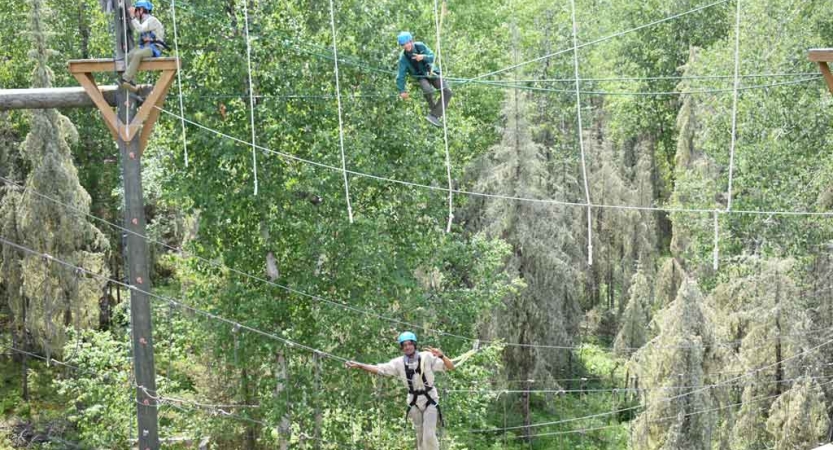two students are suspended by ropes as they make their way through a ropes course on an outward bound course